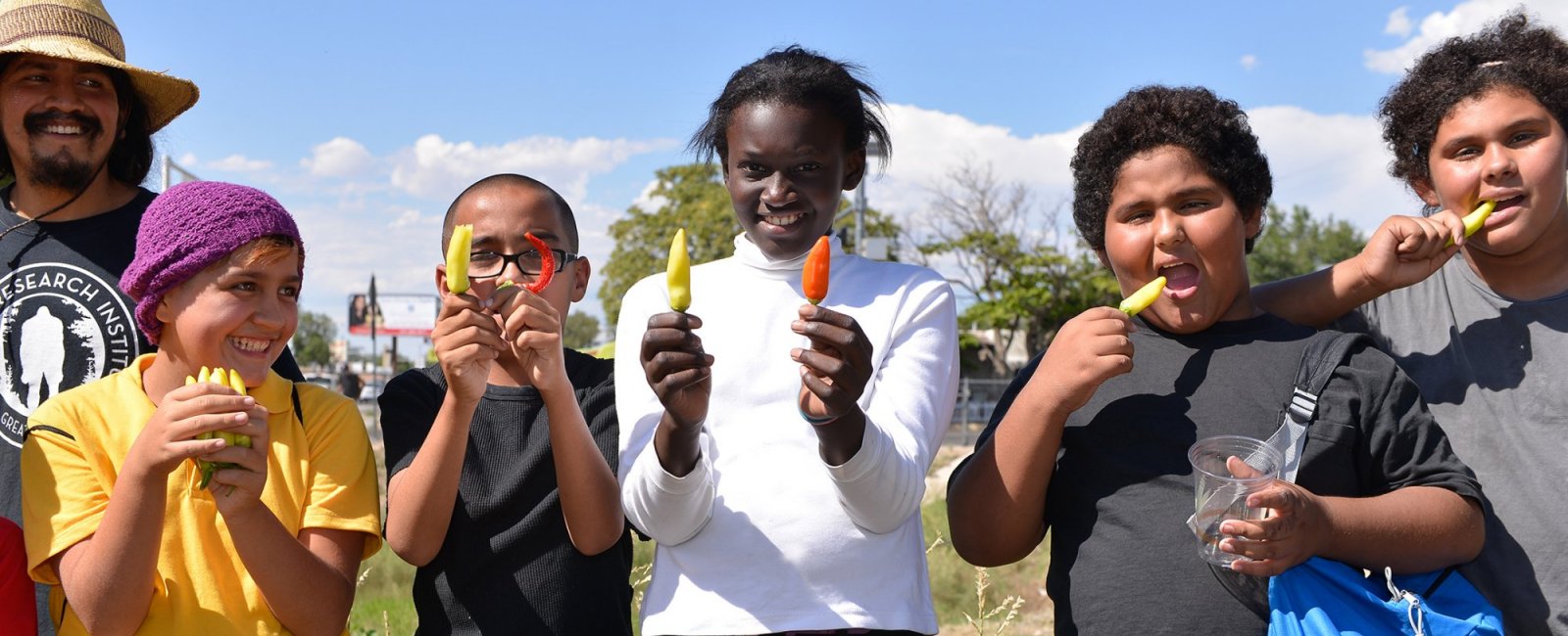 A group of kids hold up the peppers they helped grow. 